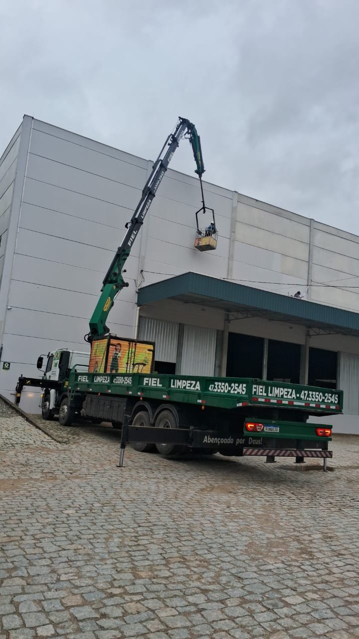 Caminhão munck do Grupo Fiel içando um cesto aéreo até a fachada de um prédio industrial
